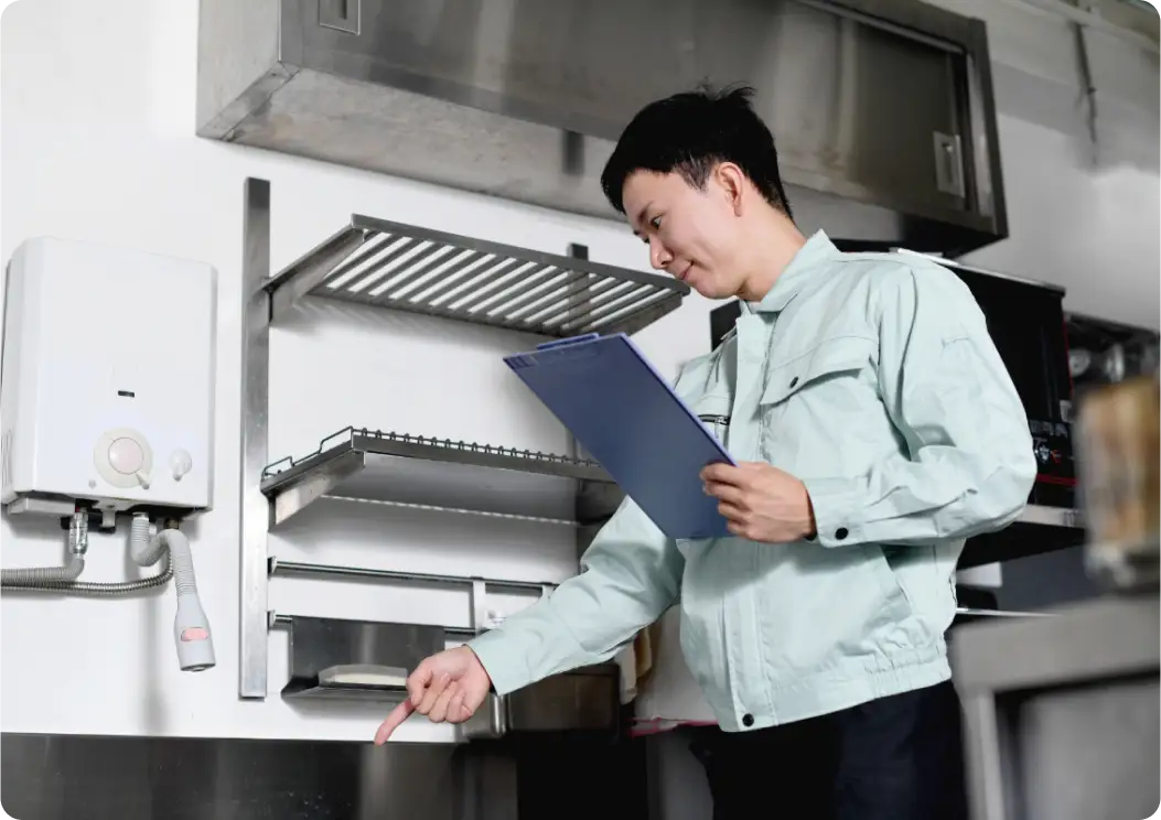 厨房で設備を確認し、シンクを指さす作業服姿の男性。