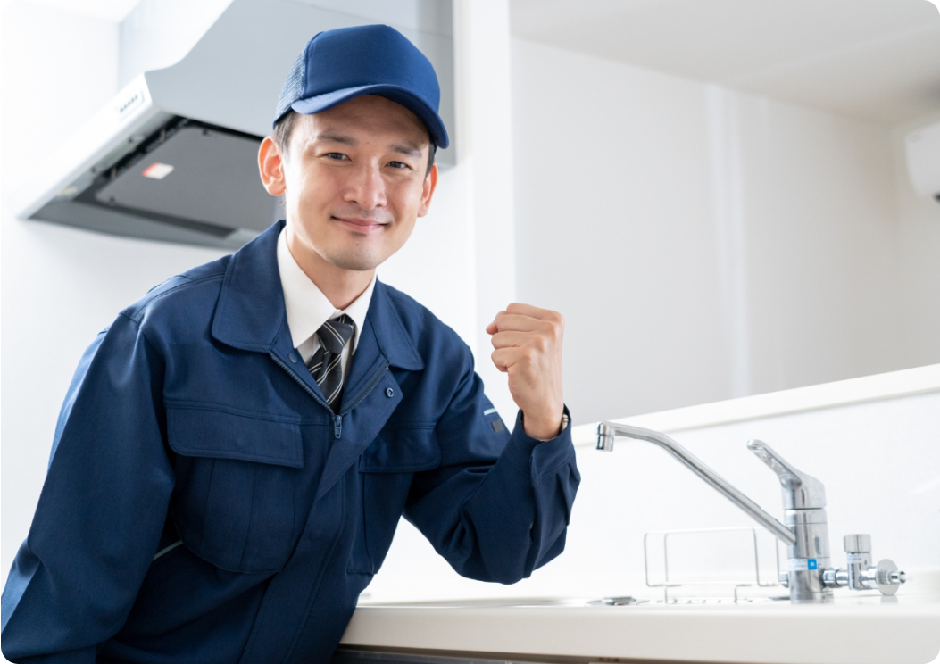 シンクの前で笑顔でポーズを取る作業服姿の男性作業員。